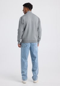 Gray sweatshirt with a high collar, textured fabric, ribbed cuffs, and waistband, paired with light blue loose-fit jeans and white sneakers.