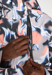 Giacca dai motivi astratti e colorati con tasca con cerniera, caratterizzata da una texture liscia e una combinazione di tonalità pastello rosa, blu e grigio.