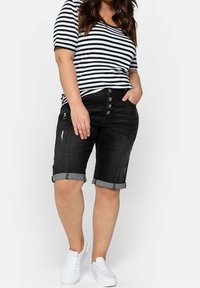 Black denim shorts with rolled hems, distressed detailing, and five button closures. Paired with a black and white striped t-shirt and white sneakers.