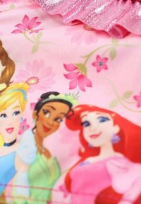 Tissu rose avec des illustrations de princesses, des motifs floraux et un volan rose brillant. Les personnages incluent Cendrillon, Tiana et Ariel.