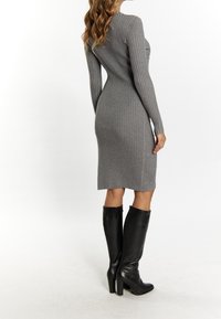 Graues, geripptes Midikleid mit langen Ärmeln, seitlichen Knopfakzenten, kombiniert mit hohen schwarzen Lederstiefeln. Glatte Textur, figurbetontes Design.