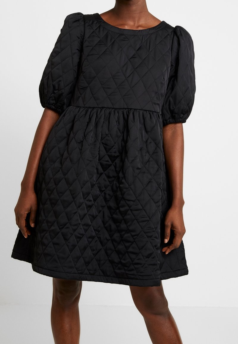 Schwarzes, gestepptes Kleid mit Puffärmeln, rundem Ausschnitt, gerafftem Bund und knielangem Saum. Das Material hat eine glatte, gepolsterte Textur.