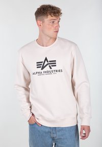 Felpa beige chiaro in tessuto morbido con scollo rotondo, caratterizzata da un logo grafico nero sul davanti. Vestibilità casual con polsini a coste.