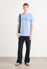 T-shirt en coton bleu clair avec le logo "BOSS" en bleu foncé, associé à un pantalon droit bleu marine. Design simple, coupe décontractée.