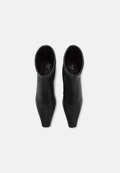 Bocanci din piele neagră la gleznă, cu un design cu vârf ascuțit, având panouri elastice pe lateral și o textură netedă. Detalii cusute de-a lungul cusăturilor.