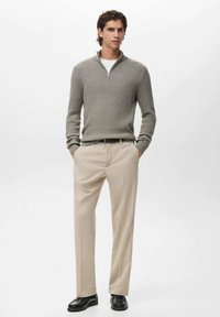 Pullover grigio a coste con colletto con zip, abbinato a pantaloni beige. Le calzature sono nere, con una finitura liscia e una suola leggermente spessa.