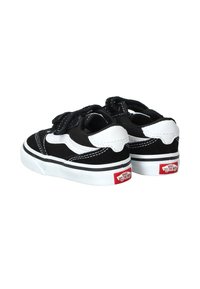 Zapatillas de lona en blanco y negro con correas de Velcro, perfil bajo, cuello acolchado, costuras blancas, suela de goma y logo rojo de Vans en el talón.