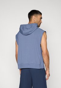 Sweat à capuche sans manches en mélange de coton bleu clair, avec capuche à cordon, coupe décontractée et ourlet côtelé. Vue de dos montrant les détails des épaules et des bras.