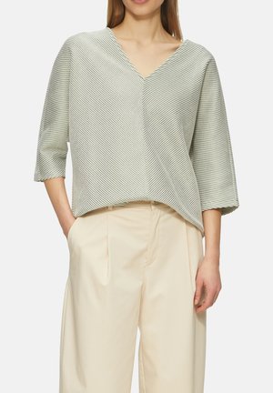 Witte en groene gestreepte blouse met een v-hals en driekwartmouwen. Zachte stof met een losse pasvorm, gedragen met beige wijde broek.