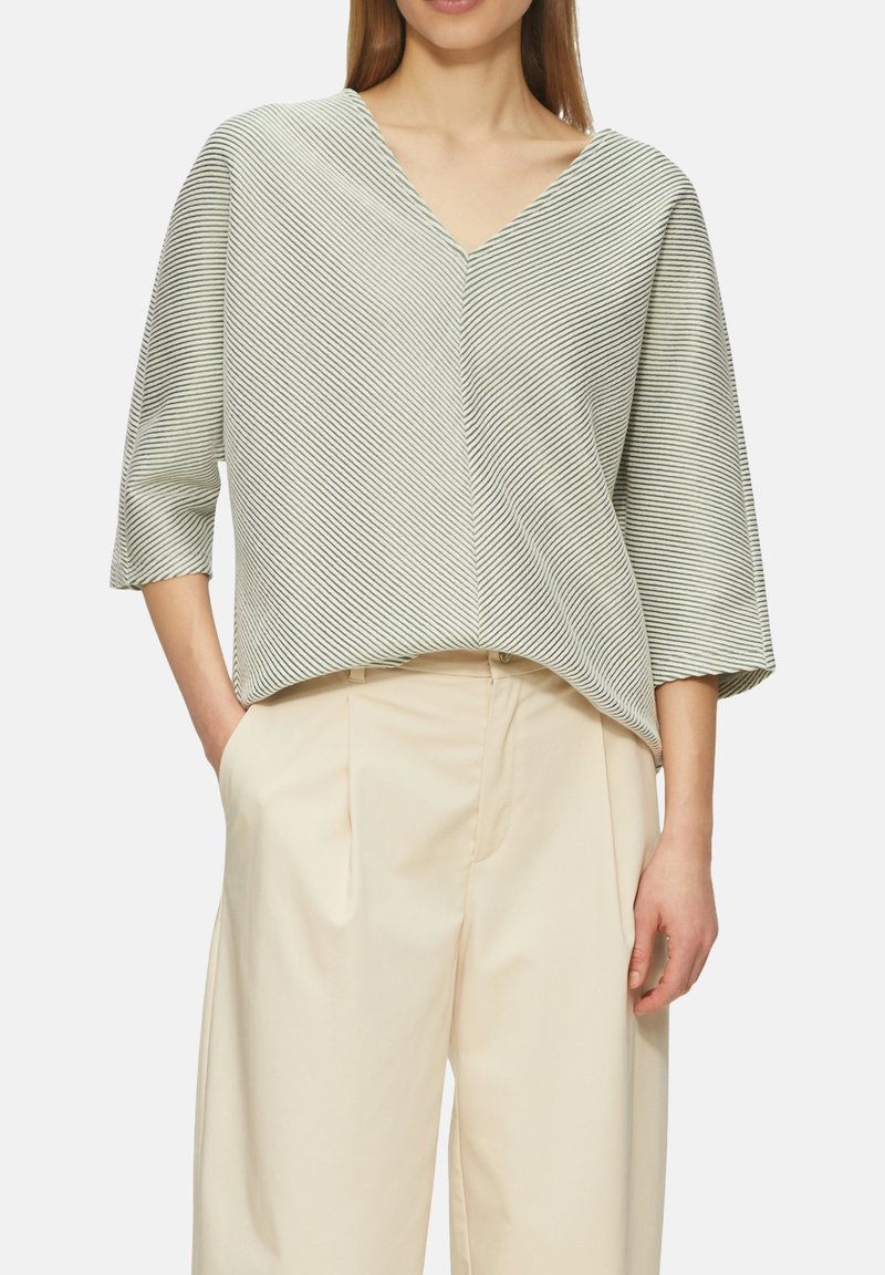 Witte en groene gestreepte blouse met een v-hals en driekwartmouwen. Zachte stof met een losse pasvorm, gedragen met beige wijde broek.