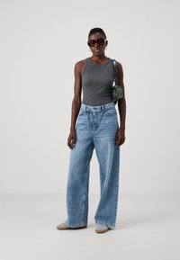 Gray tank top, loose light blue denim wide-leg jeans, gray suede shoes, black bag with green pattern, oversized sunglasses.