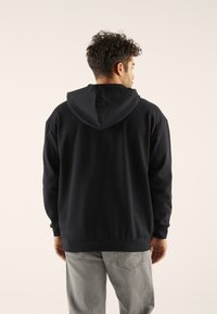 Schwarzer Kapuzenpullover mit Kängurutasche, lockerer Passform, gerippten Bündchen und Saum, getragen mit hellgrauen Jeans. Weiche Stofftextur.