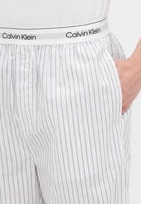 Baltie svītraini atpūtas šorti ar Calvin Klein elastīgu jostu un sānu kabatām, izgatavoti no viegla kokvilnas auduma.