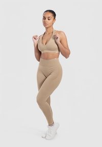 Beige sport-bh en legging set gemaakt van rekbare stof. De bh heeft een diepe V-hals en de legging heeft een hoge tailleband en een gladde textuur.