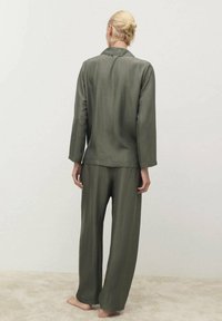 Olivegrünes Loungewear-Set mit einem Langarm-Button-Up-Oberteil und weitem Hosenbein. Weiche, glatte Textur mit lässiger Passform.