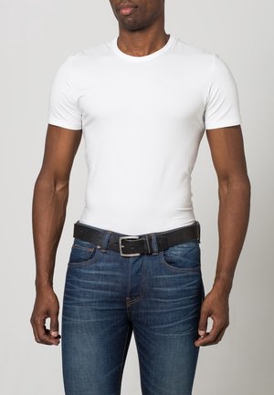 Mann trägt ein eng anliegendes, schlichtes weißes T-Shirt mit kurzen Ärmeln, in blaue Jeans gesteckt, mit einem schwarzen Ledergürtel.