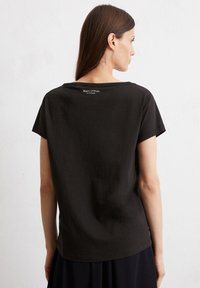 Schwarzes Baumwoll-T-Shirt mit kurzen Ärmeln, runder Ausschnitt und einem kleinen weißen Logo auf der Rückseite nahe dem Nacken.