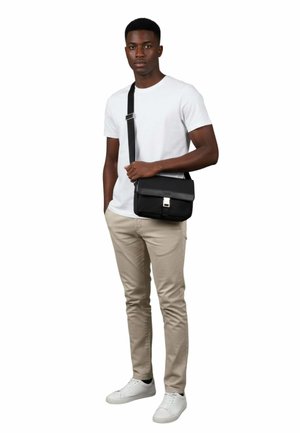 Sac bandoulière noir avec rabat, fermoir en argent et bandoulière réglable. Tissu lisse, design minimaliste, forme compacte, adaptée à un usage quotidien.