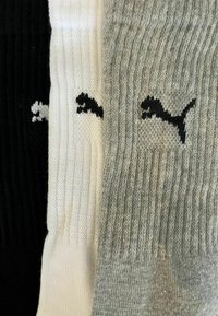 Drei Paar gerippte Socken im Crew-Stil in Schwarz, Weiß und Grau, jeweils mit einem schwarzen Puma-Logo nahe dem oberen Bündchen.
