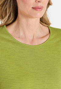 Grüner, strukturierter Oberteil mit rundem Halsausschnitt, glattem Stoff und feinem Rautenmuster, das sich auf ein eng anliegendes Design um den Hals konzentriert.