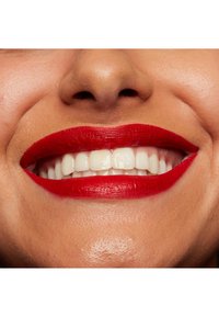 Närbild av en leende mun med vita tänder och intensivt röda läppar, som framhäver slät hudstruktur och väldefinierad läppform.