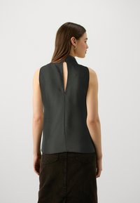 Top nero senza maniche con scollo alto e dettaglio a cuore sul retro, realizzato in tessuto liscio, abbinato a una gonna marrone scuro.