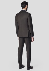 Brąsnowy garnitur o slim fit, z wyłogowym kołnierzem i pojedynczym rozcięciem. Wykonany z teksturowanej tkaniny, w zestawie z czarnymi butami.