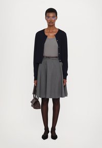 Cardigan marin, top gri fără mâneci, fustă plisată gri, curea maro, ciorapi negri, balerini negri și o geantă mică maro. Design simplu, contemporan.