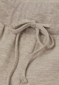 Beige Jogginghose mit Kordelzug verfügt über einen strukturierten Bund und einen weichen Stoff mit subtilen Farbvariationen. Der Kordelzug ist zu einer Schleife gebunden.