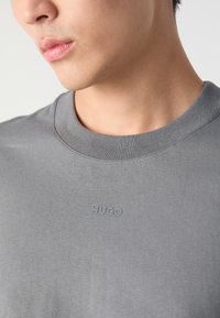 Šedé bavlněné tričko s kulatým výstřihem, s jemně vytlačeným logem "HUGO" na hrudi. Měkká textura a volný střih.