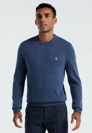 Pull en maille bleu marine avec un col rond, des poignets côtelés et une finition texturée. Présente un petit logo sur la poitrine.