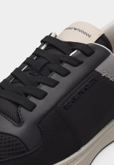 Μαύρο και γκρι αθλητικό παπούτσι Emporio Armani με μαύρα κορδόνια, υφασμάτινα πάνελ με υφή και μπεζ λεπτομέρεια στη γλώσσα με το λογότυπο.