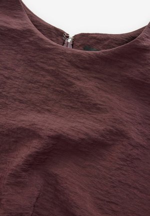 Bordeaux blouse van een gestructureerde, geweven stof. Heeft een ronde halslijn en een ritsluiting aan de achterkant. Gladde en licht gekreukte uitstraling.