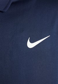 Námořnicky modré polo tričko s bílým logem Nike swoosh, vyrobené z texturované tkaniny s prodyšným síťovým vzorem.