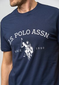 Navy blauer Baumwoll-T-Shirt mit einem weißen Grafikdesign von Polo-Spielern und dem Text "U.S. POLO ASSN. SINCE 1890". Klassischer Rundhalsausschnitt.