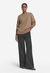 Beige Kaschmirpullover mit Rundhalsausschnitt und geripptem Saum, kombiniert mit hochtaillierten, weiten, dunkelblauen Jeans und braunen Wildlederschuhen.