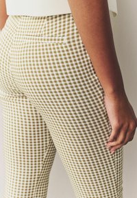 Pantalon ajusté à carreaux beige et blanc avec un petit motif à carreaux, doté d'une poche arrière et d'une texture lisse.