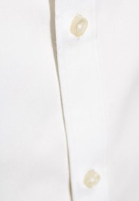 Witte overhemd met knopen, met een gladde stoftextuur, parelachtige knopen en een klassiek kraagontwerp. Close-up van de voorkant.