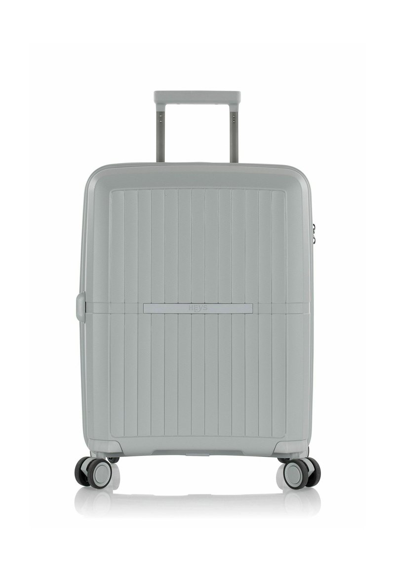 Maleta dura gris con ranuras verticales, manija retráctil y cuatro ruedas giratorias para facilitar el movimiento. Diseño elegante y superficie texturizada.