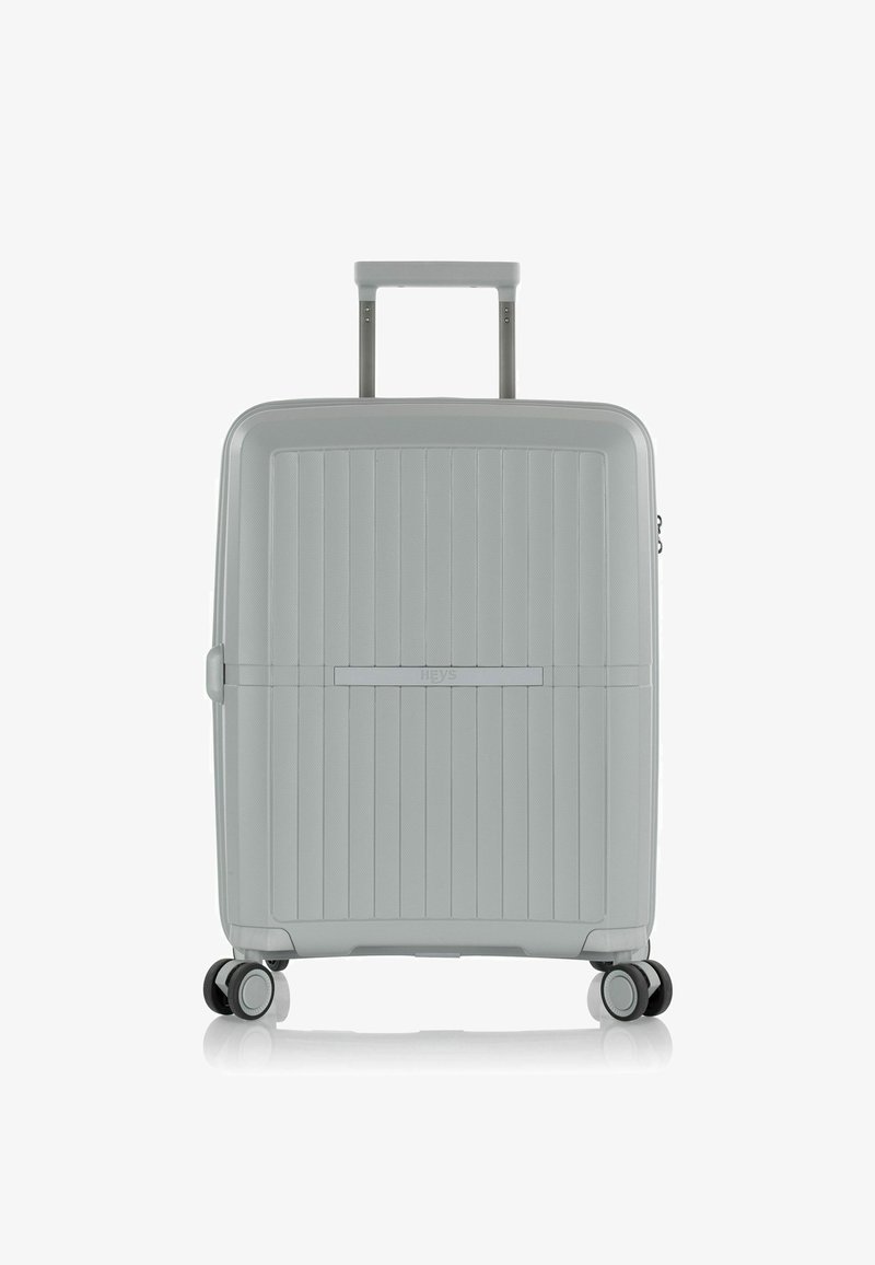 Maleta dura gris con ranuras verticales, manija retráctil y cuatro ruedas giratorias para facilitar el movimiento. Diseño elegante y superficie texturizada.