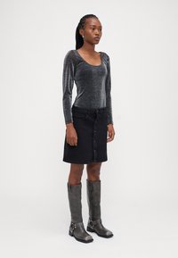 Svart denim knappekjole kombinert med en metallisk langermet topp og grå knelengde støvler. Glatte teksturer med subtil glans.