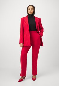 Rød dress med en skreddersydd blazer og slim-fit bukser, satt sammen med en svart høyhalset genser, og komplementert med matchende røde spisse hæler.