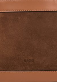 Brązowa torebka z zamszu z gładkimi skórzanymi akcentami. Posiada prosty design, wytłoczone logo marki oraz przeszycia zapewniające trwałość.