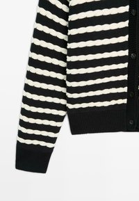 Černobíle pruhovaný kardigan s texturovaným vzorem, vyrobený z pleteného materiálu, s knoflíkovým zapínáním a žebrovanými manžetami.