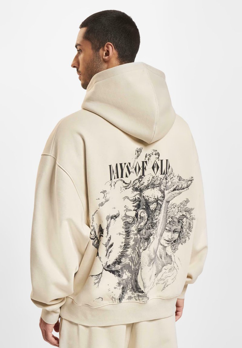 Beige oversized hettegenser med grafisk trykk på baksiden som viser klassiske figurer, med teksten "DAYS OF OLD" tydelig vist.