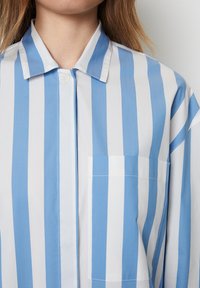 Camicia button-up con righe verticali blu e bianche, colletto e taschino sul petto, realizzata in cotone con una texture liscia.
