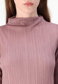 Ilga rankovė viršuje švelnaus purpurinio atspalvio su aukšta apykakle, pasižyminti banguota tekstūra ir subtiliu blizgesiu. Prigludusi fasonas pabrėžia figūrą.