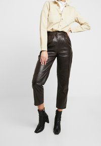 Bruna läderbyxor med hög midja och smal ben, ihop med en beige knapp-up topp och svarta ankelskor. Slät textur, avslappnad design.