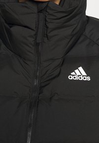 Giacca nera imbottita con colletto alto, chiusura a zip completa e logo Adidas bianco sul petto. Texture liscia e sezioni trapuntate visibili.