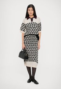 Pleteni dvoslojni outfit s crno-bijelim cvjetnim uzorkom. Bluza s kratkim rukavima i bordo ovratnikom, suknja do koljena koja prati liniju tijela i crna torba.